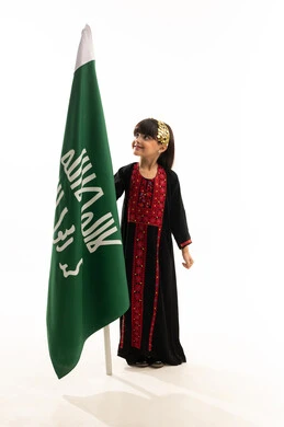 Raising children to love the homeland, the day we began 1727 AD, the northern region's costume on national occasions, looking at the flag with pride, a portrait of a smiling Saudi Gulf Arab girl wearing a muhthal holding the flag of the founding of the first Saudi state on February 22, full-length body, white background