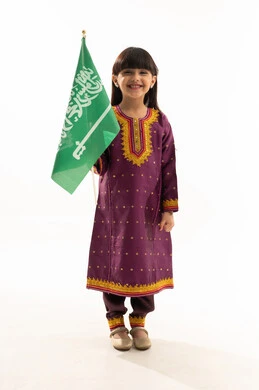 يوم العلم 11مارس، اليوم الوطني السعودي 23سبتمبر، ارتداء الأزياء الشعبية في المناسبات الوطنية, يوم بدينا 1727م, بورتريه لفتاة عربية خليجية سعودية مبتسمة تمسك علم المملكة وترتدي زي يوم تأسيس الدولة السعودية الأولى في 22 فبراير, الجسم بالطول الكامل, خلفية بيضاء