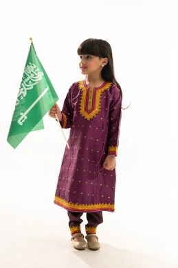 اليوم الوطني السعودي 23سبتمبر، يوم العلم 11مارس، ارتداء الأزياء الشعبية في المناسبات الوطنية, يوم بدينا 1727م, بورتريه لفتاة عربية خليجية سعودية مبتسمة تمسك علم المملكة وترتدي زي يوم تأسيس الدولة السعودية الأولى في 22 فبراير, الجسم بالطول الكامل, خلفية بيضاء