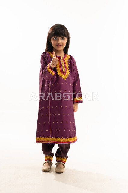 رفع اصبع الابهام بإيماءات الاعجاب، الاعتزاز بالتراث السعودي، ارتداء الأزياء الشعبية في المناسبات الوطنية, يوم بدينا 1727م, بورتريه لفتاة عربية خليجية سعودية مبتسمة ترتدي زي يوم تأسيس الدولة السعودية الأولى في 22 فبراير, الجسم بالطول الكامل, خلفية بيضاء