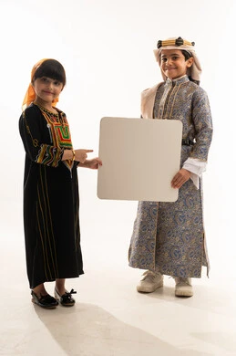 Pride in Saudi heritage, anniversary of the founding of the first Saudi state, February 22, looking at the camera with gestures of pleasure, the day we began 1727 AD, wearing traditional folk costumes, portrait of a smiling Saudi Arabian Gulf boy and girl holding a large empty white mockup, full body, white background