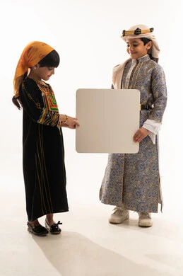 الفخر بالتراث السعودي، ذكرى تأسيس الدولة السعودية الأولى 22 فبراير، يوم بدينا 1727 م، ارتداء الازياء الشعبية التقليدية للمنططقة الجنوبية والوسطى، بورتريه لولد وبنت عربيين خليجيين سعوديين مبتسمين يحملان موك أب أبيض فارغ كبير، الجسم بالطول الكامل، خلفية بيضاء