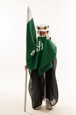 تربية الأبناء على حب الوطن، ارتداء أزياء المنطقة الشرقية في اليوم الوطني 23سبتمبر، يوم بدينا 1727 م، بورتريه لولد عربي خليجي سعودي مبتسم يرتدي البشت والغترة وعقال التأسيس يقوم بتقبيل علم تأسيس الدولة السعودية 22 فبراير، صورة لكامل الجسم، خلفية بيضاء