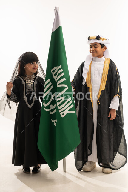 تربية الأبناء على الحب والولاء للوطن، زي تراثي سعودي للمناسبات الوطنية، يوم بدينا 1727 م، بورتريه لولد وبنت عربيين خليجيين سعوديين مبتسمين يمسكان علم تأسيس الدولة السعودية الأولى 22 فبراير، ، الجسم بالطول الكامل، خلفية بيضاء