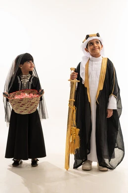 صناعات يدوية شعبية، النظر إلى الاعلى بايماءات السعادة، زي تراثي سعودي للمناسبات الوطنية، تأسيس الدولة السعودية الأولى 22 فبراير، يوم بدينا 1727 م، بورتريه لولد وبنت عربيين خليجيين سعوديين مبتسمين يحملان سيف ذهبي وسلة قش، الجسم بالطول الكامل، خلفية بيضاء