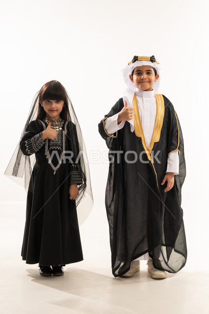 Thumbs up gesture, reviving Saudi heritage, Saudi traditional costume for national occasions, founding of the first Saudi state, February 22, the day we began 1727 AD, portrait of a smiling Saudi Arabian Gulf boy and girl, full body, white background