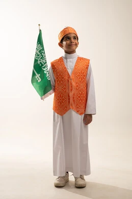 Saudi National Day commemoration September 23, Flag Day March 11, wearing Western Region costumes on a national occasion, Badina Day 1727 AD, portrait of a smiling Saudi Gulf Arab boy wearing the traditional Sudairi holding the flag, founding of the first Saudi state February 22, full body photo, white background