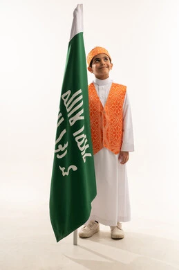 التباهي والفخر بالتراث السعودي، ارتداء أزياء المنطقة الغربية في الاحتفالات والمناسبات الوطنية، يوم بدينا 1727 م، بورتريه لولد عربي خليجي سعودي مبتسم يرتدي السديري الشعبي يمسك علم تأسيس الدولة السعودية الأولى 22 فبراير، صورة الجسم بالكامل, خلفية بيضاء