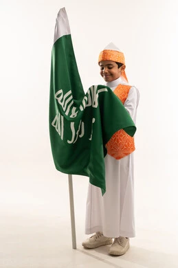 تربية الأبناء على حب الوطن، النظر إلى العلم بإيماءات الفخر، ارتداء أزياء المنطقة الغربية في مناسبة وطنية، يوم بدينا 1727 م، بورتريه لولد عربي خليجي سعودي مبتسم يرتدي السديري الشعبي يمسك علم تأسيس الدولة السعودية الأولى 22 فبراير، صورة الجسم بالكامل, خلفية بيضاء