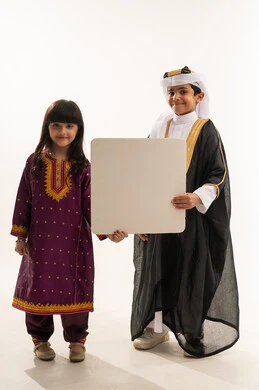 اليوم الوطني السعودي، ذكرى تأسيس الدولة السعودية الأولى 22 فبراير، النظر إلى الكاميرا بإيماءات السرور، يوم بدينا 1727 م، ارتداء الازياء الشعبية التقليدية، بورتريه لولد وبنت عربيين خليجيين سعوديين مبتسمين يحملان موك أب أبيض فارغ كبير، الجسم بالطول الكامل، خلفية بيضاء