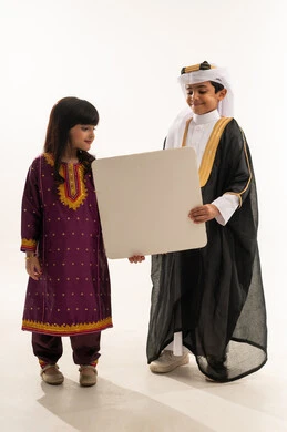 يوم بدينا 1727 م، اليوم الوطني السعودي، ذكرى تأسيس الدولة السعودية الأولى 22 فبراير، ارتداء الازياء الشعبية التقليدية، بورتريه لولد وبنت عربيين خليجيين سعوديين مبتسمين يحملان موك أب أبيض فارغ كبير، الجسم بالطول الكامل، خلفية بيضاء