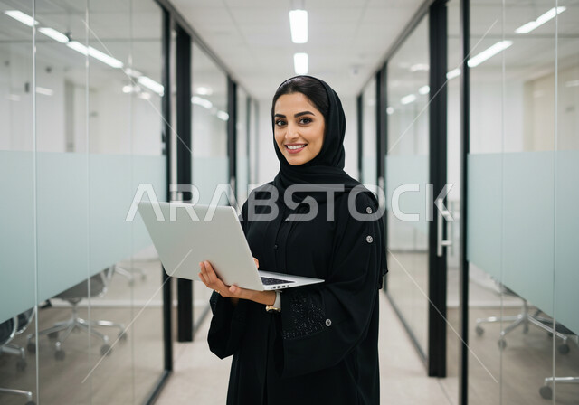  مهن ووظائف نسائية مكتبية سعودية، ادارة وانجاز المهام باستخدام جهاز تقني حديث ومتطور, إمرأة عربية خليجية سعودية مبتسمة ترتدي الحجاب والعباءة تعمل على الحاسوب المحمول في مقر الشركة, ايماءات وتعابير السرور والسعادة