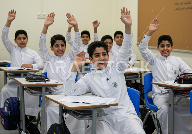 أهداف التربية والتعليم في المملكة العربية السعودية، أساليب التعلم الفعال والمشاركة مع المعلم، موسم العودة إلى المدارس، مجموعة من الطلاب العرب الخليجيين السعوديين يرتدون الزي المدرسي يجلسون في مقاعدهم يقومون برفع ايديهم للاجابة