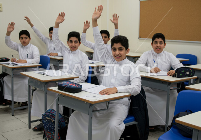 أهداف التربية والتعليم في المملكة العربية السعودية، أساليب التعلم الفعال والمشاركة مع المعلم، موسم العودة إلى المدارس، مجموعة من الطلاب العرب الخليجيين السعوديين يرتدون الزي المدرسي يجلسون في مقاعدهم يقومون برفع ايديهم للاجابة