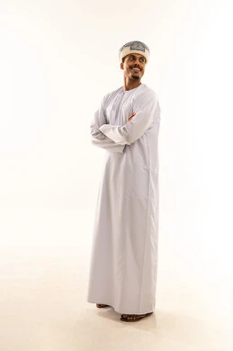 Looking at something, the concept of masculinity and dignity, attention to external appearance, expressions of self-confidence, a portrait of a smiling Omani Gulf Arab man wearing a dishdasha and a turban, standing with arms crossed, full-body, white background.