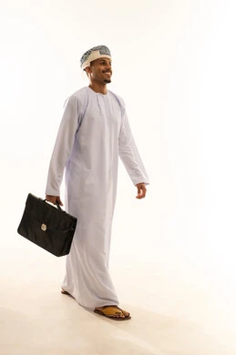 المشي نحو الأمام بثقة وثبات، ايماءات المشي و الذهاب إلى مكان معين، بورتريه من الجانب لرجل عربي خليجي عماني مبتسم يرتدي الدشداشة و العمامة يحمل بيديه حقيبه العمل، صورة الجسم بالطول الكامل، خلفية بيضاء