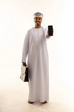عرض شاشة سوداء فارغة، استخدام جهاز تقني حديث، ، بورتريه لرجل عربي خليجي عماني يرتدي الدشداشة و العمامة يمسك بيده حقيبه العمل والهاتف المحمول ينظر إلى الكاميرا بإيماءات السرور،الجسم بالطول الكامل، خلفية بيضاء