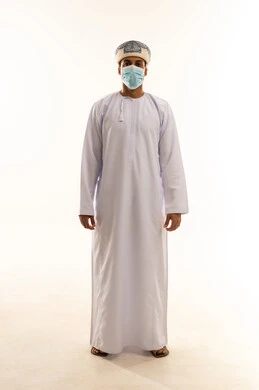 مفهوم الاناقة و الاهتمام بالمظهر الخارجي, بورتريه لشاب عربي خليجي عماني يرتدي الدشداشة و العمامة و الكمامة يقف باستقامة، تعابيرالثقه بالنفس, الجسم بالطول الكامل، خلفية بيضاء