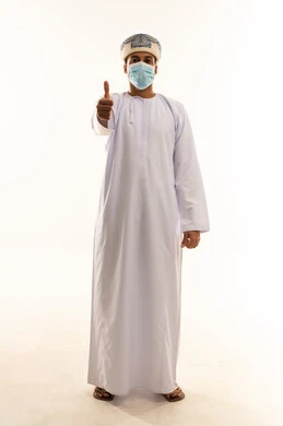 الموافقة على أمر معين، ايماءات الرضا والسرور والسعادة، حركات الاعجاب والقبول, بورتريه لرجل عربي خليجي عماني يرتدي الدشداشة و العمامة و الكمامة ينظر الى الكاميرا يرفع اصبعه الإبهام للأعلى بتعابير علامة الجودة, الجسم بالطول الكامل، خلفية بيضاء