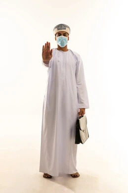 مفهوم الرفض والامتناع والانزعاج, بورتريه لرجل عربي خليجي عماني يرتدي الدشداشة و العمامة و الكمامة يحمل حقيبه العمل يمد يده نحو الأمام مع رفع الكف بإيماءات النهي عن فعل امر ما, طلب التوقف وعدم الاقتراب, تعابير الحزم والجدية, الجسم بالطول الكامل، خلفية بيضاء