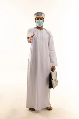 مفهوم الترحيب و السلام و إلقاء التحية، بورتريه لرجل عربي خليجي عماني يرتدي الدشداشة و العمامة و الكمامة يمسك حقيبه عمل يقوم بمد يده نحو الأمام ، حركات يدين تدل على المصافحة، الطول الكامل للجسم، خلفية بيضاء