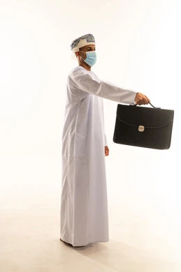 الاهتمام بالمظهر الخارجي، بورتريه من الجانب لرجل عربي خليجي عماني يرتدي الدشداشة و العمامة و الكمامة يحمل بيده حقيبة العمل ينظر أمامه بإيماءات الثقة بالنفس، مفهوم إداة الأعمال والمشاريع، الجسم بالطول الكامل، خلفيه بيضاء