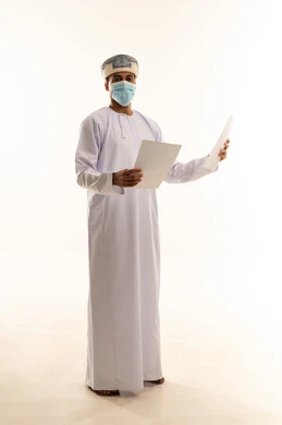 اعداد التقارير الخاصة بالعمل، بورتريه لشاب عربي خليجي عماني يرتدي الدشداشة و العمامة و الكمامة يحمل بيده مجموعة من الاوراق البيضاء، مراجعة ومتابعة الخطط والمشاريع المكتبية ، الجسم بالطول الكامل ، خلفية بيضاء