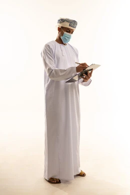 مهنة ووظيفة شبابية، التدقيق على التقرير الشهري، القيام بأداء المهام اليومية المكتبيه, بورتريه  لرجل عربي خليجي عماني يرتدي العمامة و الدشداشة و الكمامة يحمل بيده قلم وورقة يقوم بكتابة شيء ما, الجسم بالطول الكامل ، خلفية بيضاء