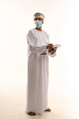 التدقيق على التقرير الشهري، القيام بأداء المهام اليومية المكتبيه, بورتريه  لرجل عربي خليجي عماني يرتدي العمامة و الدشداشة و الكمامة يحمل بيده قلم وورقة ينظر الى شيء ما, مهنة ووظيفة شبابية, الجسم بالطول الكامل ، خلفية بيضاء