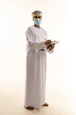 Performing daily office tasks, a portrait of an Arab Gulf Omani man wearing a turban, dishdasha, and mask, holding a pen and paper, looking at the camera with gestures of joy, a youthful profession and job, reviewing the monthly report, full-body shot, white background.