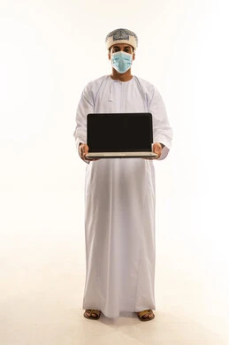 عرض شاشة سوداء فارغة، استخدام الأجهزة والتقنيات الحديثة المتطورة، تصفح مواقع التواصل الاجتماعي, بورتريه لرجل عربي خليجي عماني يرتدي الدشداشة و العمامة و الكمامة يحمل بيده الحاسوب المحمول  ينظر إلى الكاميرا بإيماءات السعادة والسرور, الجسم بالطول الكامل، خلفية بيضاء