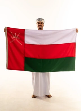 إظهار الولاء و الاخلاص والانتماء للبلاد، أعياد ومناسبات وطنية، الاحتفال باليوم الوطني العماني 18 نوفمبر، بورتريه لشاب عربي خليجي عماني يرتدي مبتسم العمامة والدشداشة يمسك العلم بايماءات الفخر ، مفهوم حب الوطن، الجسم بالطول الكامل، خلفية بيضاء