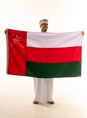 أعياد ومناسبات وطنية، الاحتفال باليوم الوطني العماني 18 نوفمبر، إظهار الولاء و الاخلاص والانتماء للبلاد، بورتريه لشاب عربي خليجي عماني يرتدي مبتسم العمامة والدشداشة يمسك العلم بايماءات الفخر و ينظر الى شي ما، مفهوم حب الوطن، الجسم بالطول الكامل، خلفية بيضاء