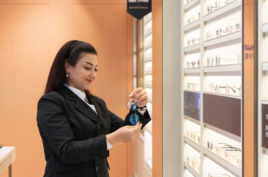 تحسين الرؤية ومحاولة تعديل البصر، شابة عربية خليجية اماراتيه ترتدي الزي الرسمي تقوم باختيار نظارة طبية ملائمة لملامح الوجه، صورة من الجانب لامرأة سعوديه تقوم بشراء النظارات الخاصة بضعف وقصرالنظر، متعة التسوق في الأسواق والمحلات الإماراتية