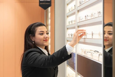 Keeping up with the latest fashion trends, using optics to clarify vision, a young Saudi Arabian Gulf woman wearing a formal dress choosing eyeglasses that fit her facial features, a close-up of an Emirati woman buying glasses for nearsightedness and myopia, the joy of shopping in Emirati stores