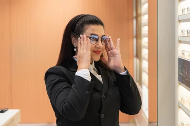 Shopping and buying from Emirati stores, expressions of self-confidence, the concept of weak eyesight, purchasing new eyeglasses, a close-up of a veiled Saudi Arabian Gulf woman wearing formal attire choosing eyeglasses that suit her facial features, an Emirati woman examining eyeglasses
