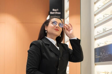 الاعجاب بالنظارات الطبية الجديدة، تصحيح وتحسين الرؤية، مفهوم ضعف النظر، صورة مقربة لسيدة عربية خليجية سعودية ترتدي الزي الرسمي تقوم باختيار نظارة ملائمة لملامح الوجه، امرأة إماراتية تقوم بمعاينة النظارات، متعة التسوق والشراء من المحلات الإماراتية