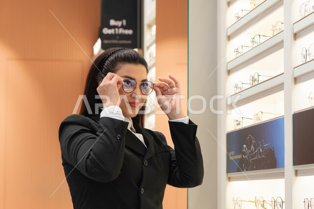 الأناقة والاهتمام بالمظهر الخارجي، مفهوم الرؤية الواضحة، ماركات عالمية فاخرة، صورة مقربة لسيدة عربية خليجية اماراتيه ترتدي الزي الرسمي تقوم باختيار نظارة ملائمة لملامح الوجه، امرأة سعوديه تقوم بمعاينة النظارات، الاعجاب بالنظارات الطبية الجديدة، ضعف ونقص النظر