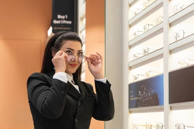 مفهوم الرؤية الواضحة، ماركات عالمية فاخرة، صورة مقربة لسيدة عربية خليجية اماراتيه ترتدي الزي الرسمي تقوم باختيار نظارة ملائمة لملامح الوجه، امرأة سعوديه تقوم بمعاينة النظارات، الاعجاب بالنظارات الطبية الجديدة، ضعف ونقص النظر