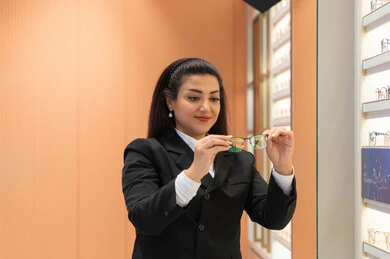 التأثير الإيجابي للتسوق على المرأة، الاعجاب بالنظارات الطبية الجديدة، تصحيح وتحسين الرؤية، مفهوم ضعف النظر، صورة مقربة لسيدة عربية خليجية سعودية ترتدي الزي الرسمي تقوم باختيار نظارة ملائمة لملامح الوجه، امرأة إماراتية تقوم بمعاينة النظارات