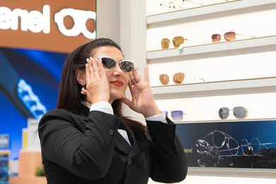 Modern women's accessories, interest in outward appearance, the positive impact of shopping on women, trying on sunglasses before buying, an Emirati woman choosing suitable sunglasses, a Saudi Arabian Gulf woman wearing formal attire trying on her glasses