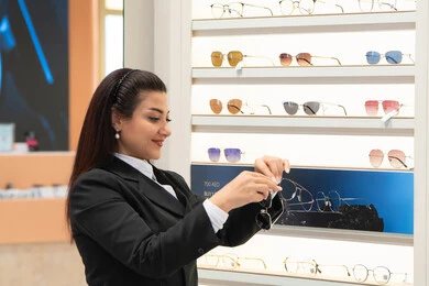 السرور والمتعة بالتسوق في مولات الإمارات، مواكبة آخر صيحات الموضة والجمال، أحدث الاكسسوارات النسائية العصرية الأنيقة، صورة مقربة لسيدة عربية خليجية اماراتية ترتدي الزي الرسمي تقوم باختيار نظارة شمسية ملائمة لملامح الوجه، امرأة سعودية تقوم بمعاينة النظارات