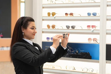 متابعة آخر صيحات الموضة والجمال، أحدث الاكسسوارات النسائية العصرية الأنيقة، السرور والمتعة بالتسوق في مولات الإمارات، صورة مقربة لسيدة عربية خليجية اماراتية ترتدي الزي الرسمي تقوم باختيار نظارة شمسية ملائمة لملامح الوجه، امرأة سعودية تقوم بمعاينة النظارات