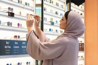 Keeping up with the latest fashion and beauty trends, the latest stylish women's accessories, the joy of shopping in the UAE malls, a Saudi woman examining colored glasses, a side view of a veiled young Emirati Gulf Arab woman wearing an abaya choosing sunglasses that suit her facial features