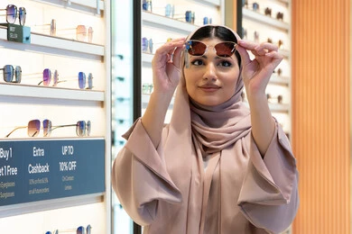 Buying stylish, modern women's accessories, keeping up with the latest fashion and beauty trends, enjoying shopping in the UAE malls, a Saudi woman examining colored glasses, a veiled young Emirati Gulf Arab woman wearing an abaya choosing sunglasses that suit her facial features