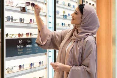 The pleasure and enjoyment of shopping in the Emirates malls, keeping up with the latest fashion and beauty trends, the latest elegant and modern women's accessories, a close-up of a veiled young Arab Gulf Emirati woman wearing an abaya choosing sunglasses that suit her facial features, a Saudi woman examining glasses