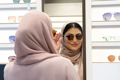 Caring about one's appearance, the pleasure of shopping in the Emirates, modern women's accessories, choosing suitable sunglasses, an Emirati woman trying on glasses before buying, a close-up photo from the back of a veiled Saudi Arabian Gulf young woman wearing an abaya trying on her glasses and looking at them in the mirror