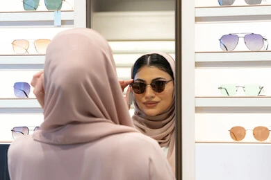 Enjoying shopping in the Emirates, taking care of one's appearance, modern women's accessories, choosing suitable sunglasses, an Emirati woman trying on glasses before buying, a close-up photo from the back of a veiled Saudi Arabian Gulf young woman wearing an abaya trying on her glasses and looking at them in the mirror