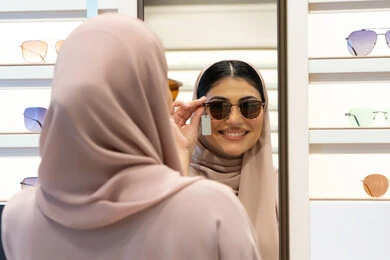 The joy of shopping in the Emirates, modern women's accessories, choosing suitable sunglasses, taking care of one's appearance, an Emirati woman trying on glasses before buying, a close-up photo from the back of a veiled Saudi Arabian Gulf young woman wearing an abaya trying on her glasses and looking at them in the mirror