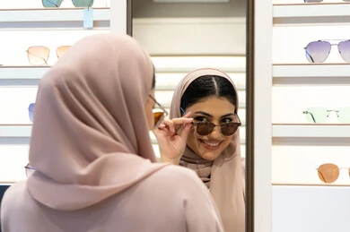 Gestures of happiness and pleasure, enjoying shopping in the Emirates, trendy women's accessories, choosing suitable sunglasses, Emirati woman trying on glasses before buying, close-up from the back of a veiled Saudi Arabian Gulf young woman wearing an abaya trying on her glasses and looking at them in the mirror